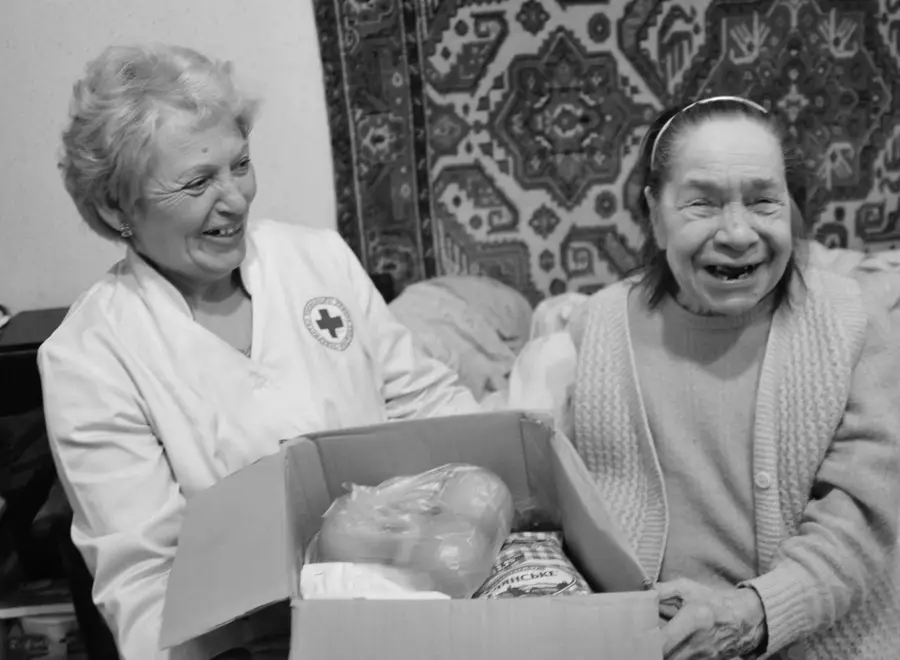 Pflegerin und Seniorin lachen über einem Paket mit Lebensmitteln